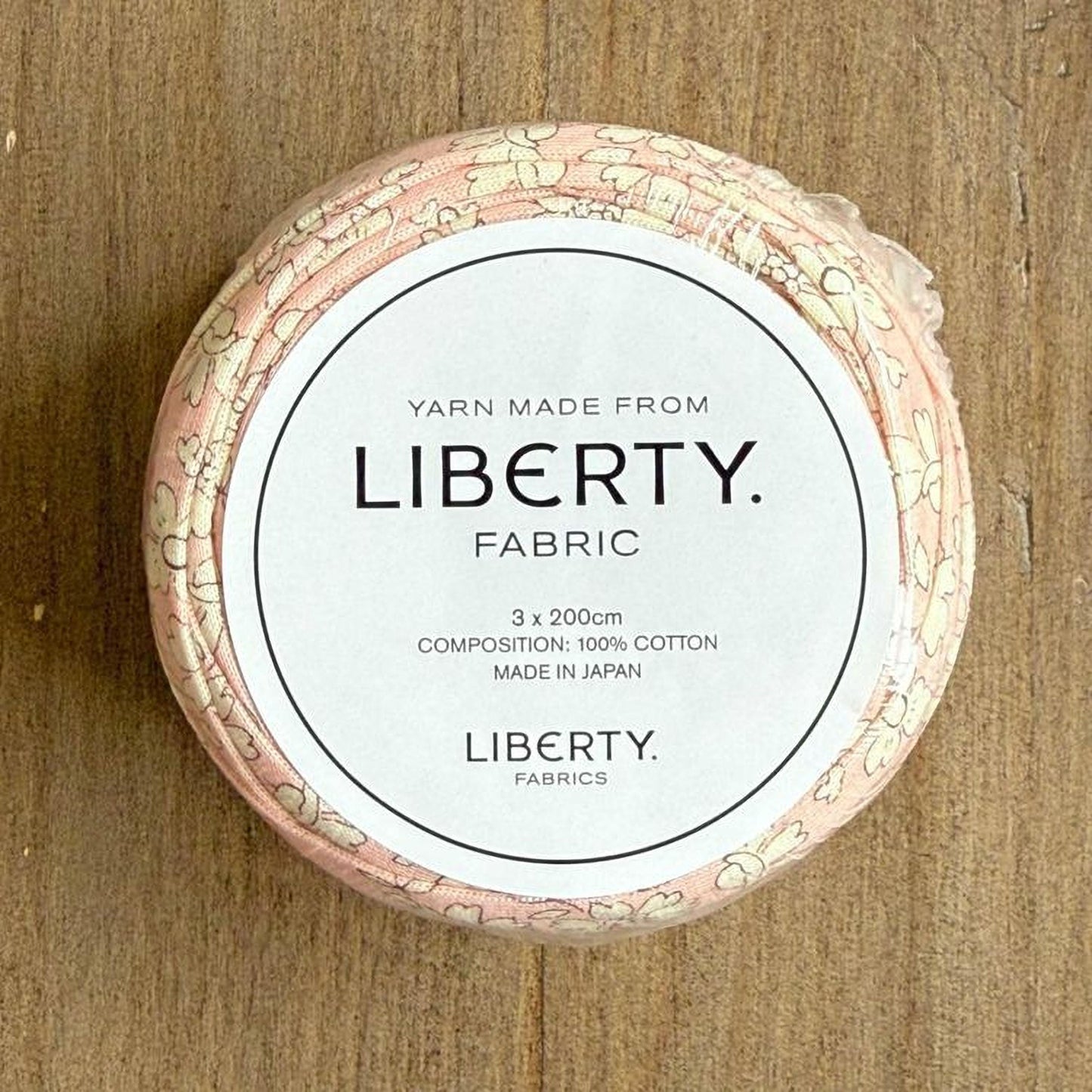 A spool of yarn made from Liberty fabric, with a label indicating it is composed of 100% cotton and is made in Japan.