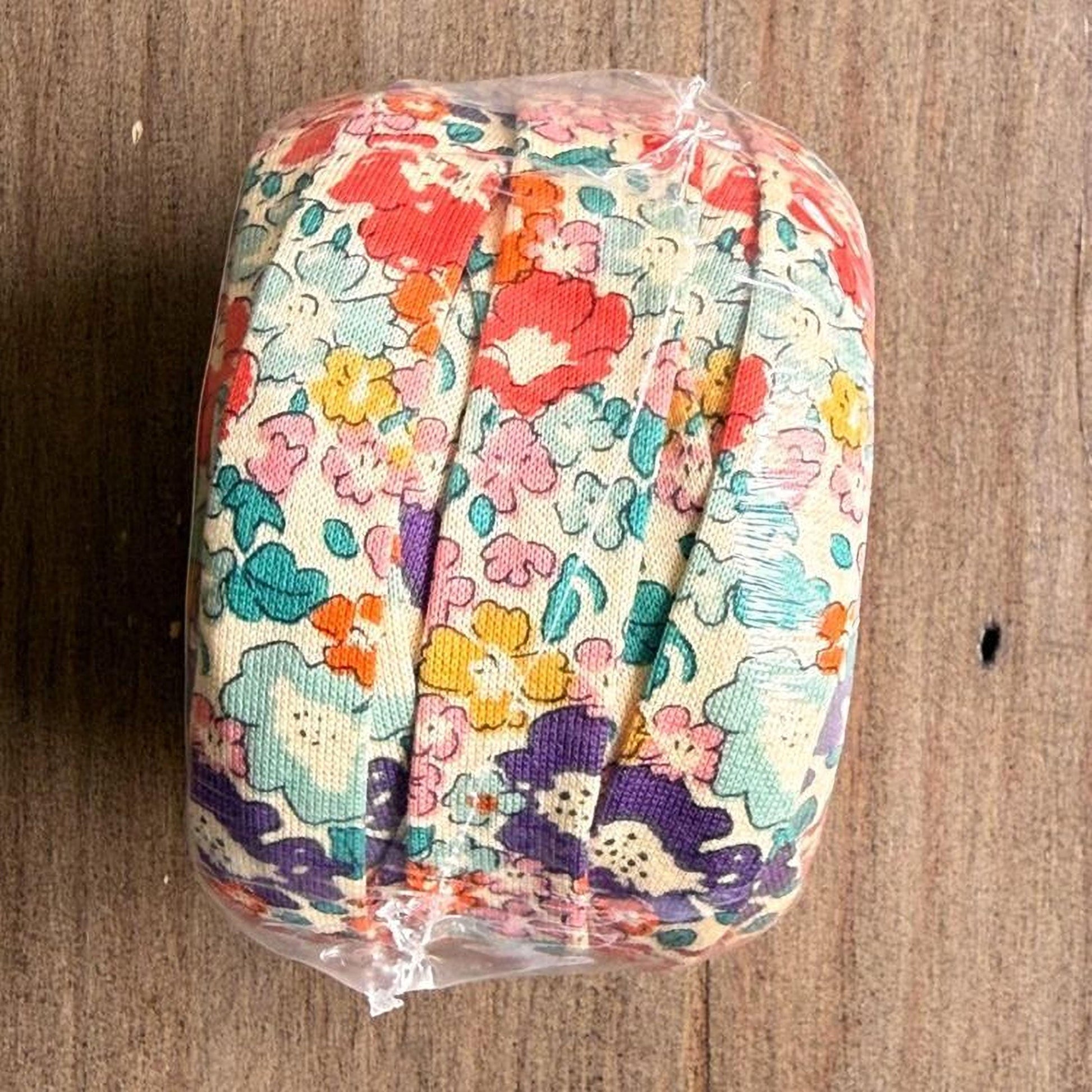 A colorful floral fabric is wrapped in plastic and placed on a wooden surface.