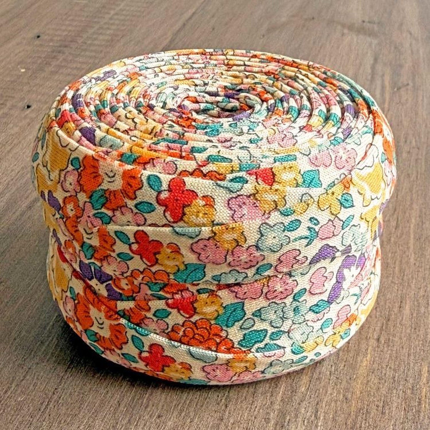 A colorful, floral-patterned fabric item, possibly a quilt or a decorative piece, is displayed on a wooden surface.