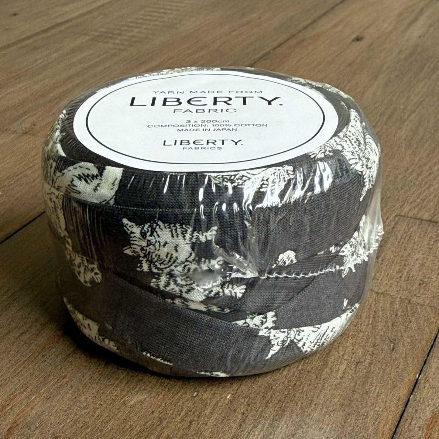 A roll of Liberty fabric, which is a type of yarn made from cotton, is sitting on a wooden surface.
