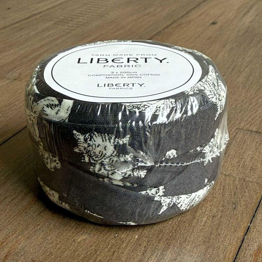 A roll of Liberty fabric, which is a type of yarn made from cotton, is sitting on a wooden surface.