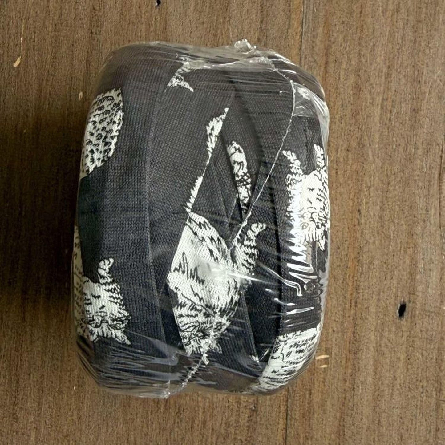 A black and white cat patterned fabric is wrapped in clear plastic, sitting on a wooden surface.