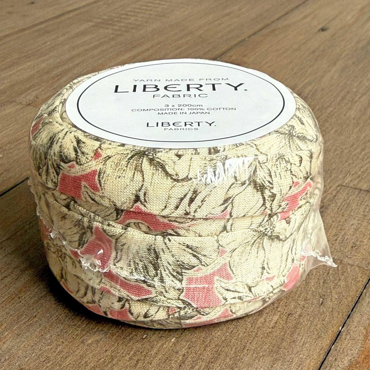 A package of Liberty fabric, which is a type of cotton fabric, is sitting on a wooden surface.