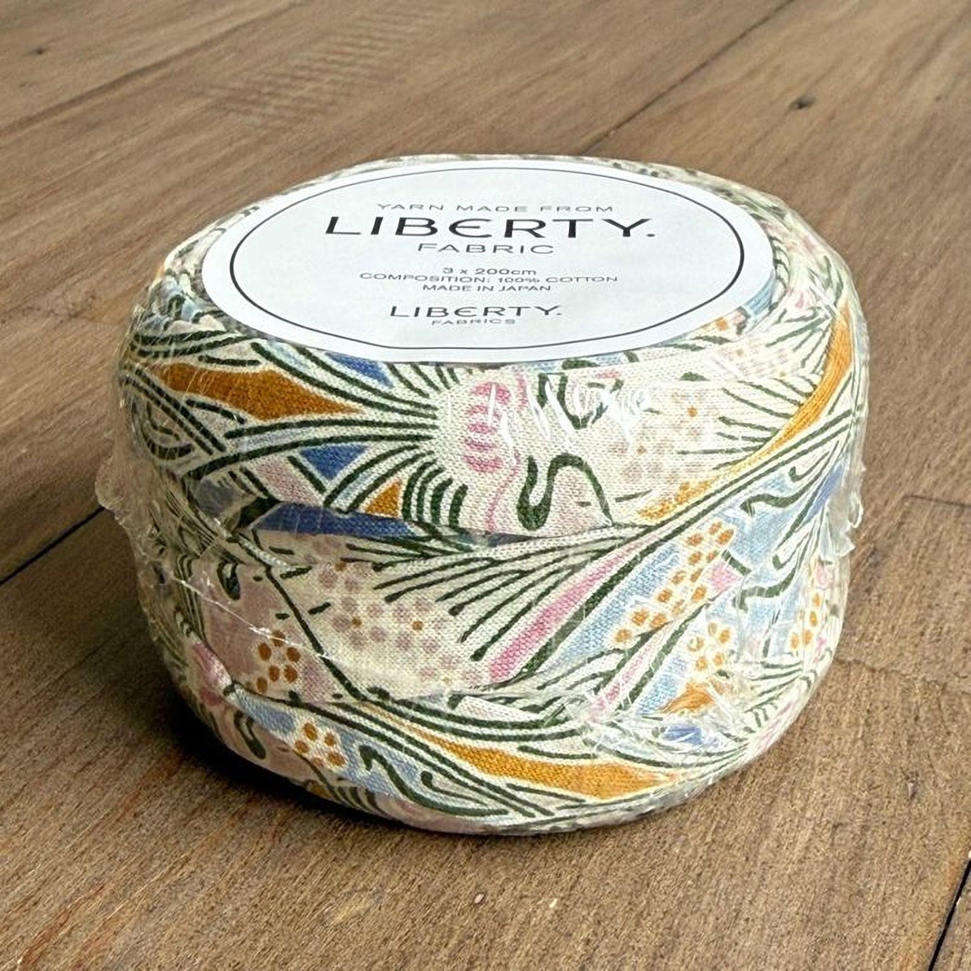 A package of Liberty yarn made from fabric, sitting on a wooden surface.