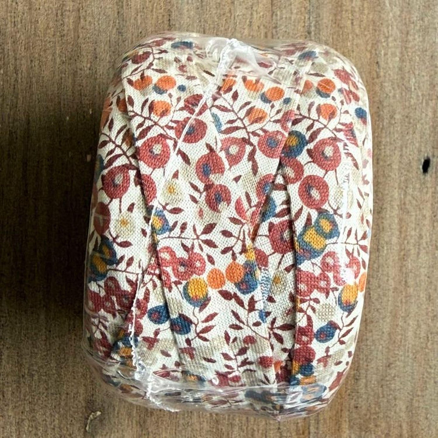 A roll of fabric with a floral pattern is wrapped in plastic and placed on a wooden surface.