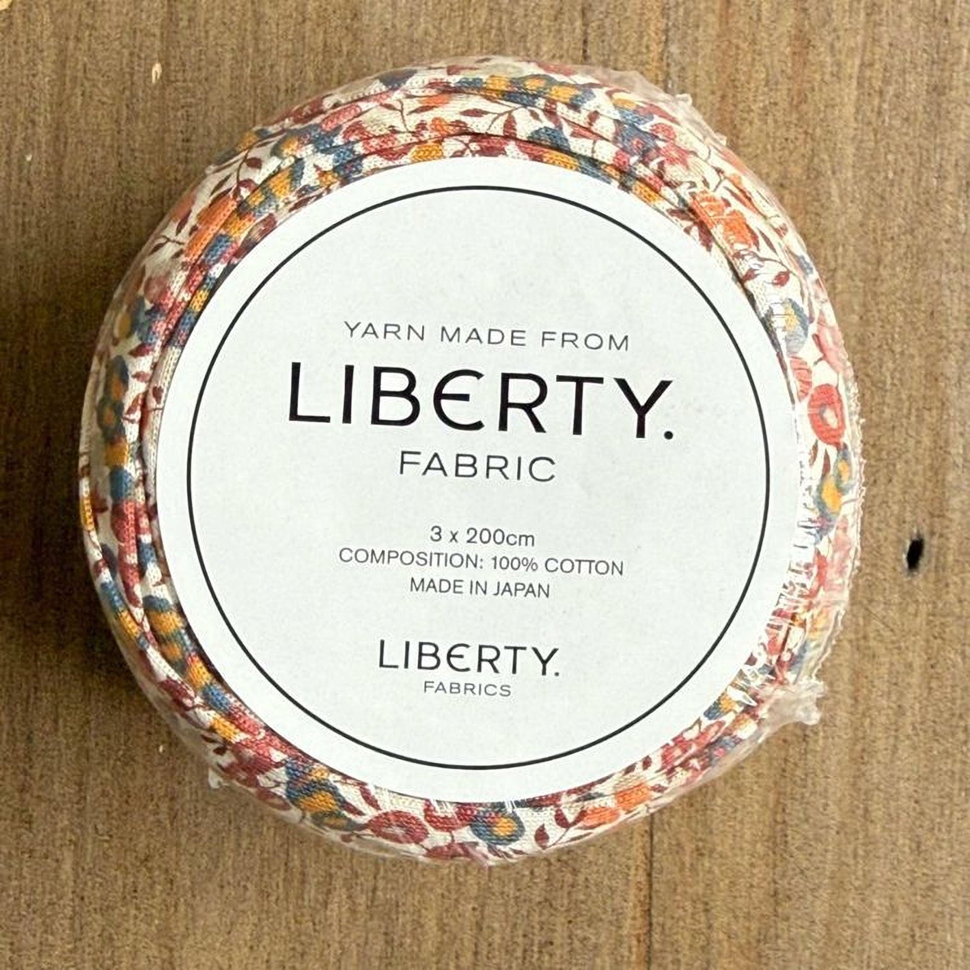 A circular container with a label that reads "Yarn Made from LIBERTY. FABRIC" and provides details about the product, including its composition and manufacturing origin.