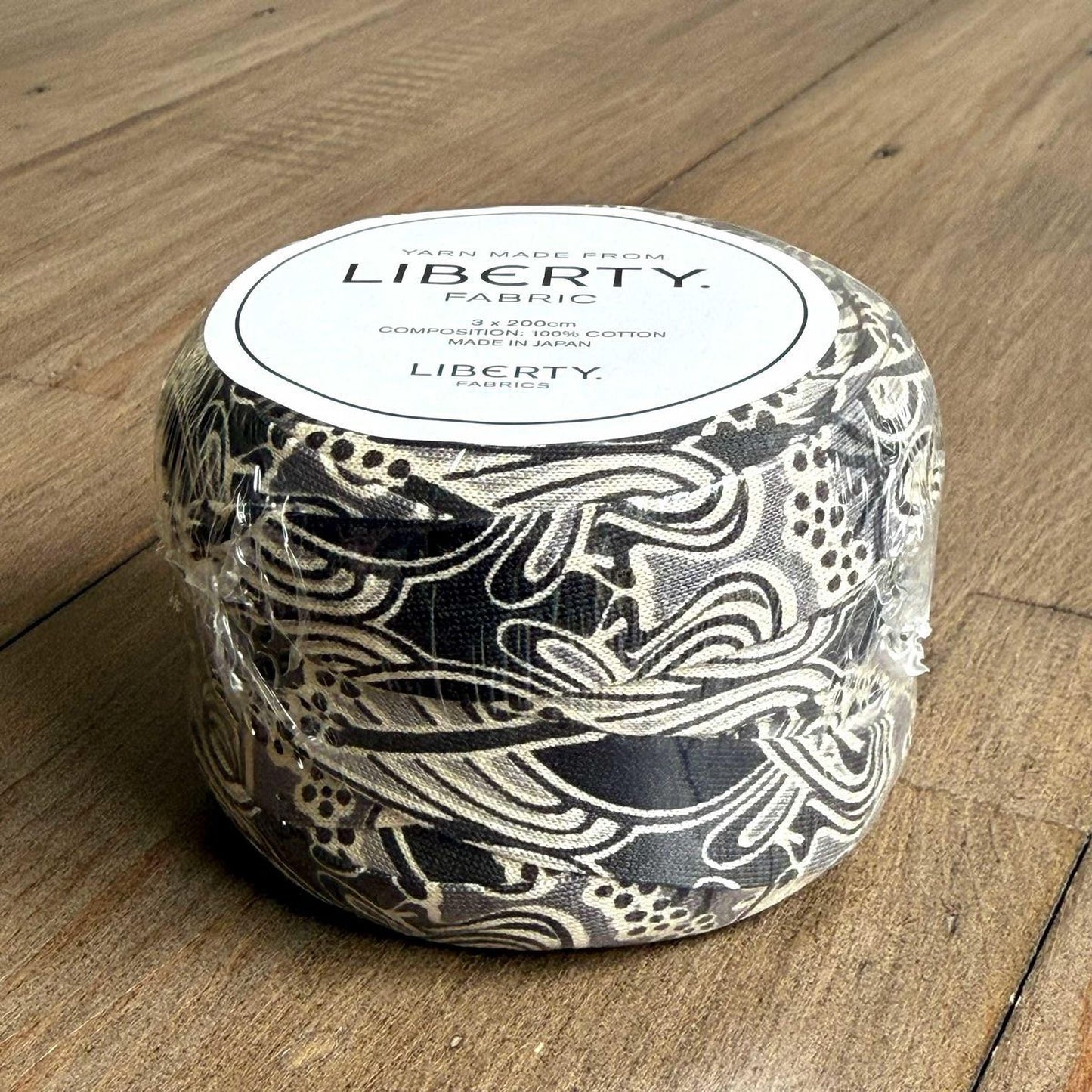 A black and white fabric with a floral pattern is wrapped in plastic and placed on a wooden surface.