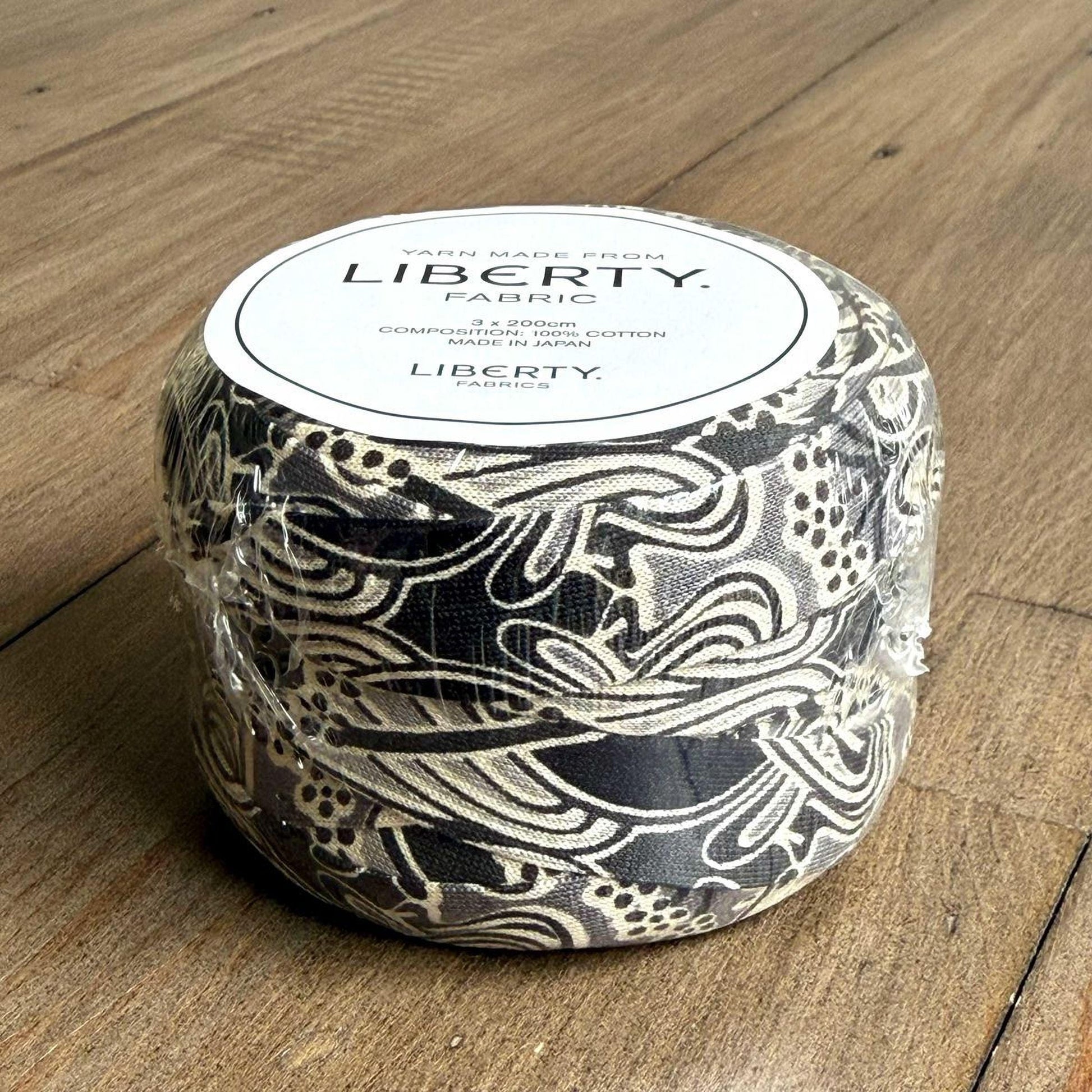 A black and white fabric with a floral pattern is wrapped in plastic and placed on a wooden surface.