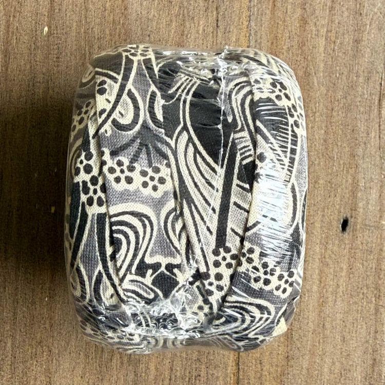 A black and white patterned fabric item wrapped in plastic, sitting on a wooden surface.