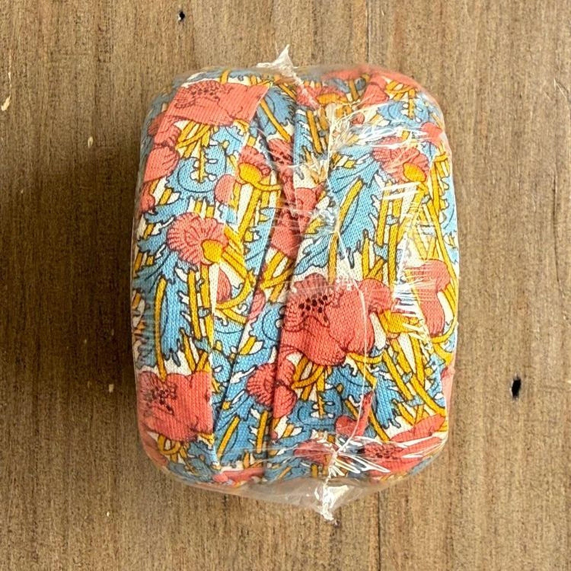 A colorful, patterned object wrapped in plastic, sitting on a wooden surface.