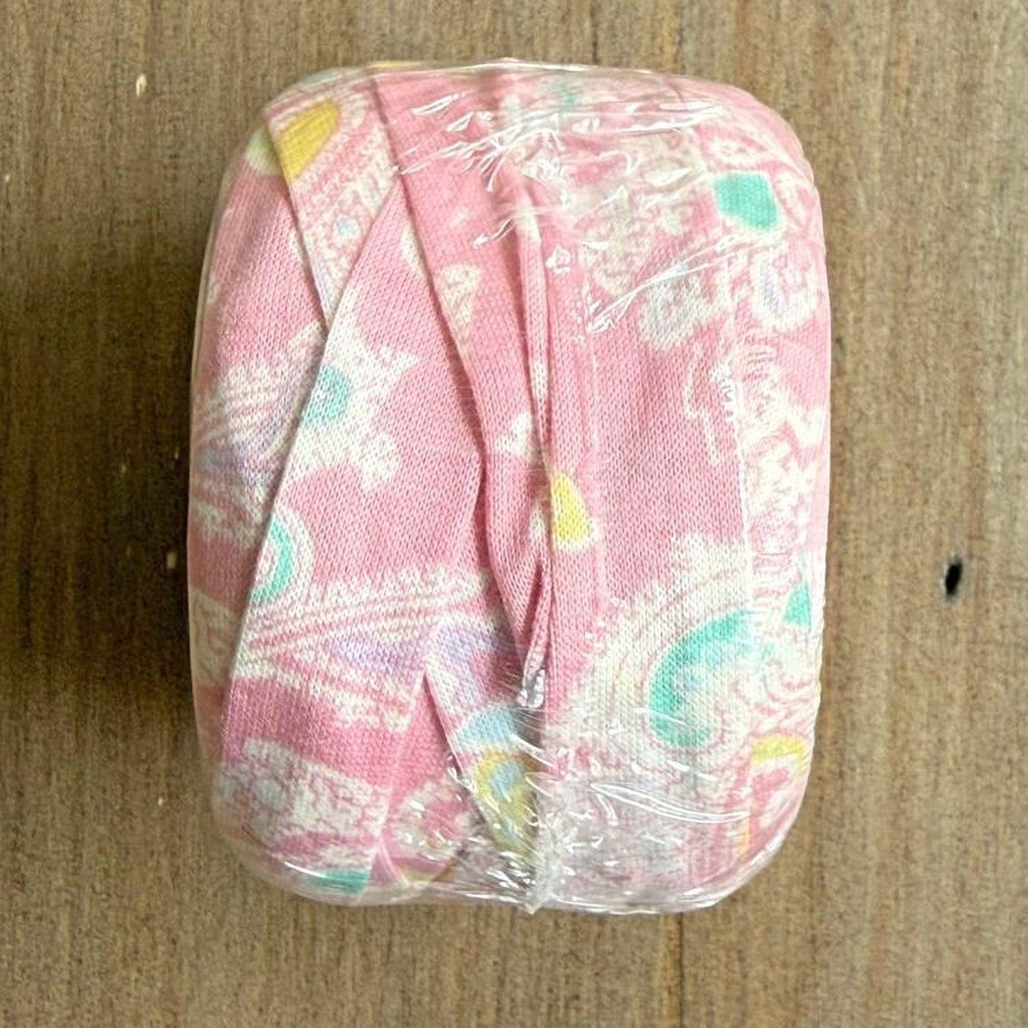 A pink fabric with a floral pattern is wrapped in clear plastic, sitting on a wooden surface.
