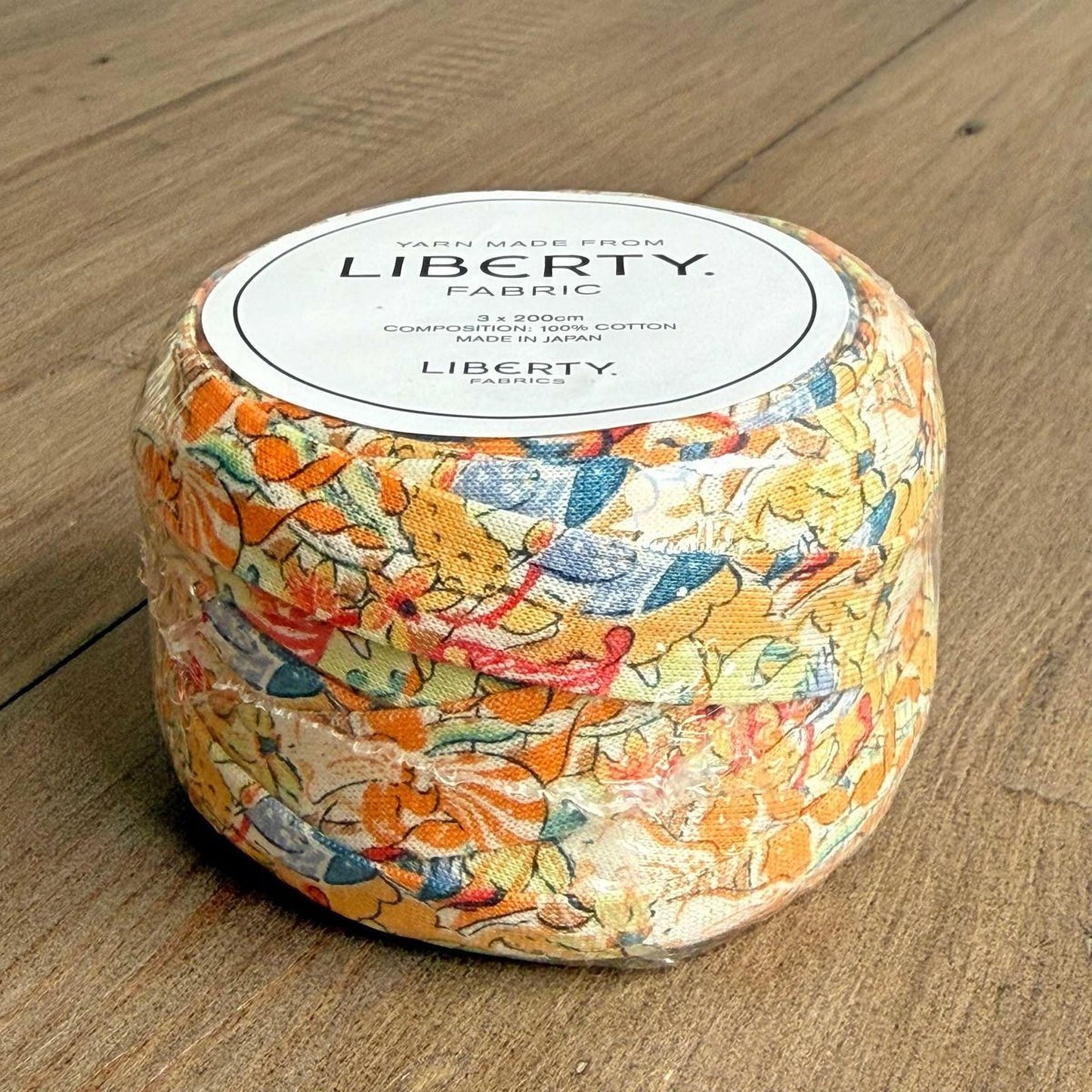 A package of Liberty fabric, featuring a colorful floral pattern, is displayed on a wooden surface.