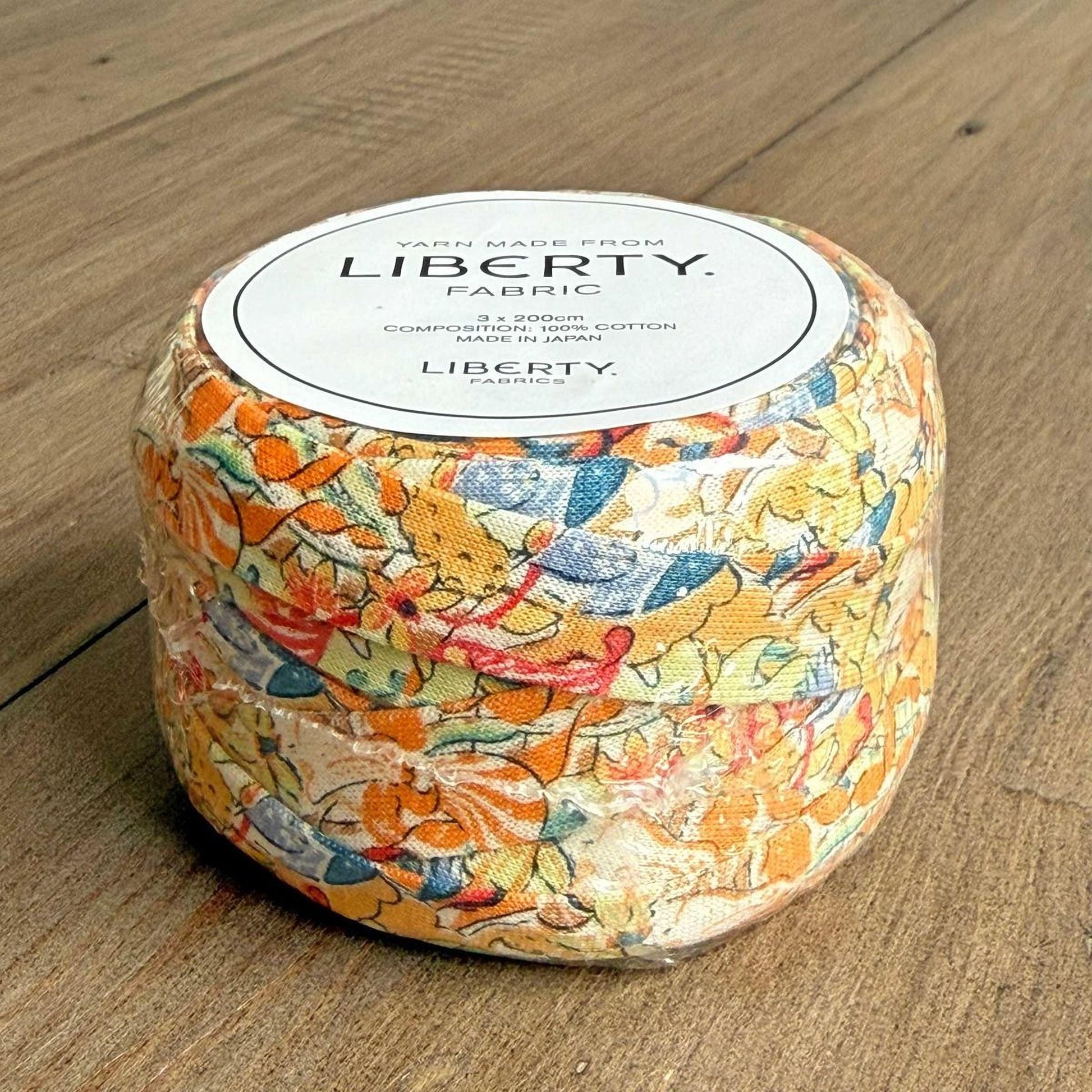 A package of Liberty fabric, featuring a colorful floral pattern, is displayed on a wooden surface.