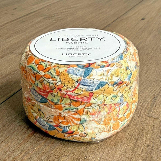 A package of Liberty fabric, featuring a colorful floral pattern, is displayed on a wooden surface.