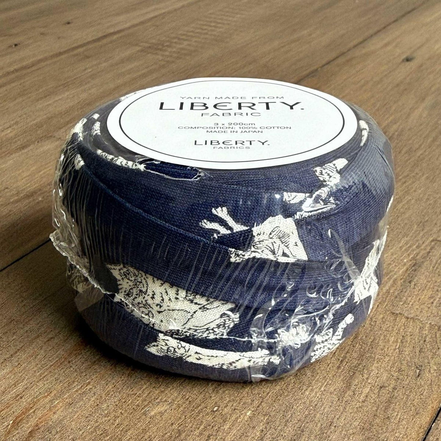 A blue and white fabric item wrapped in plastic, sitting on a wooden surface.