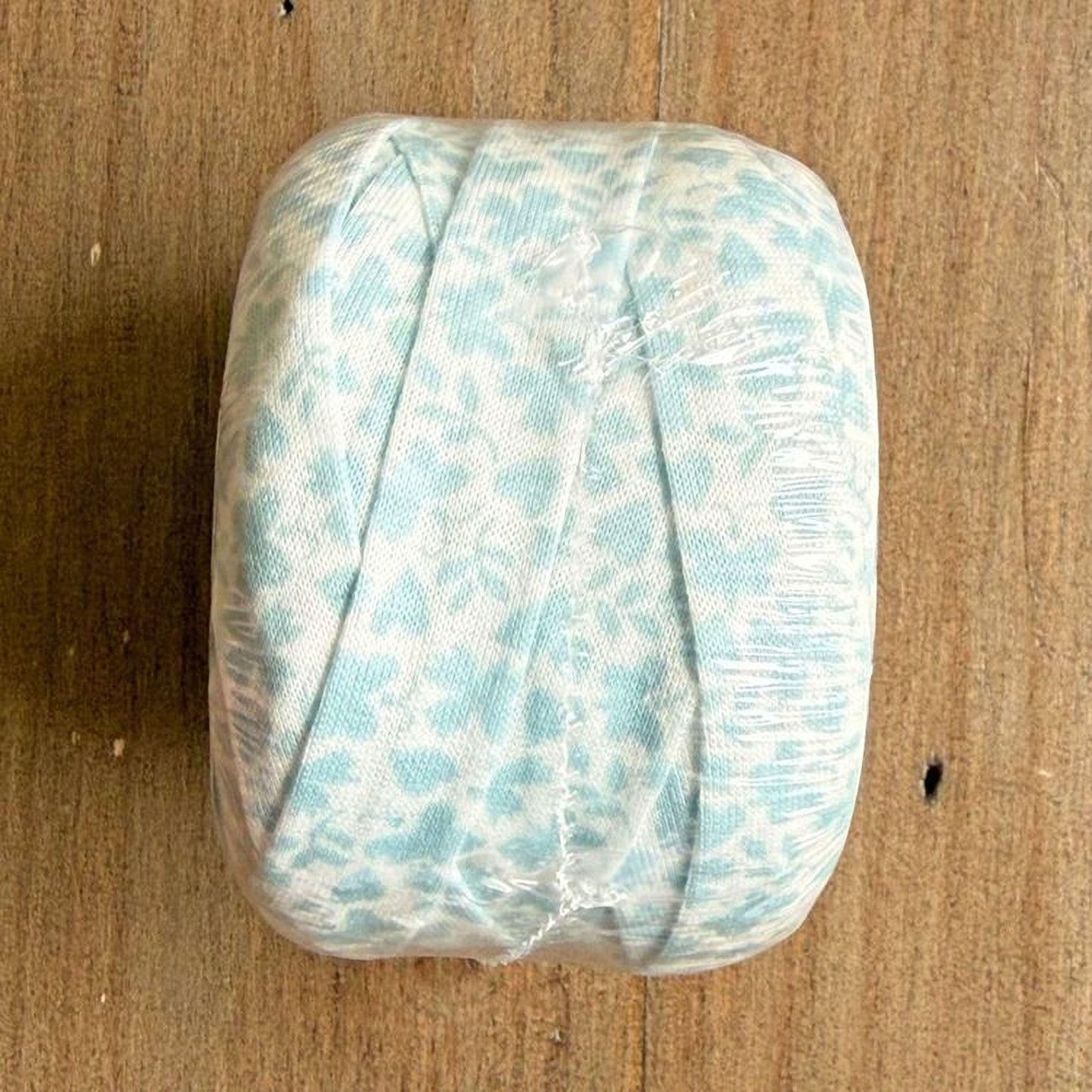 A light blue fabric with a white floral pattern is wrapped in plastic and placed on a wooden surface.