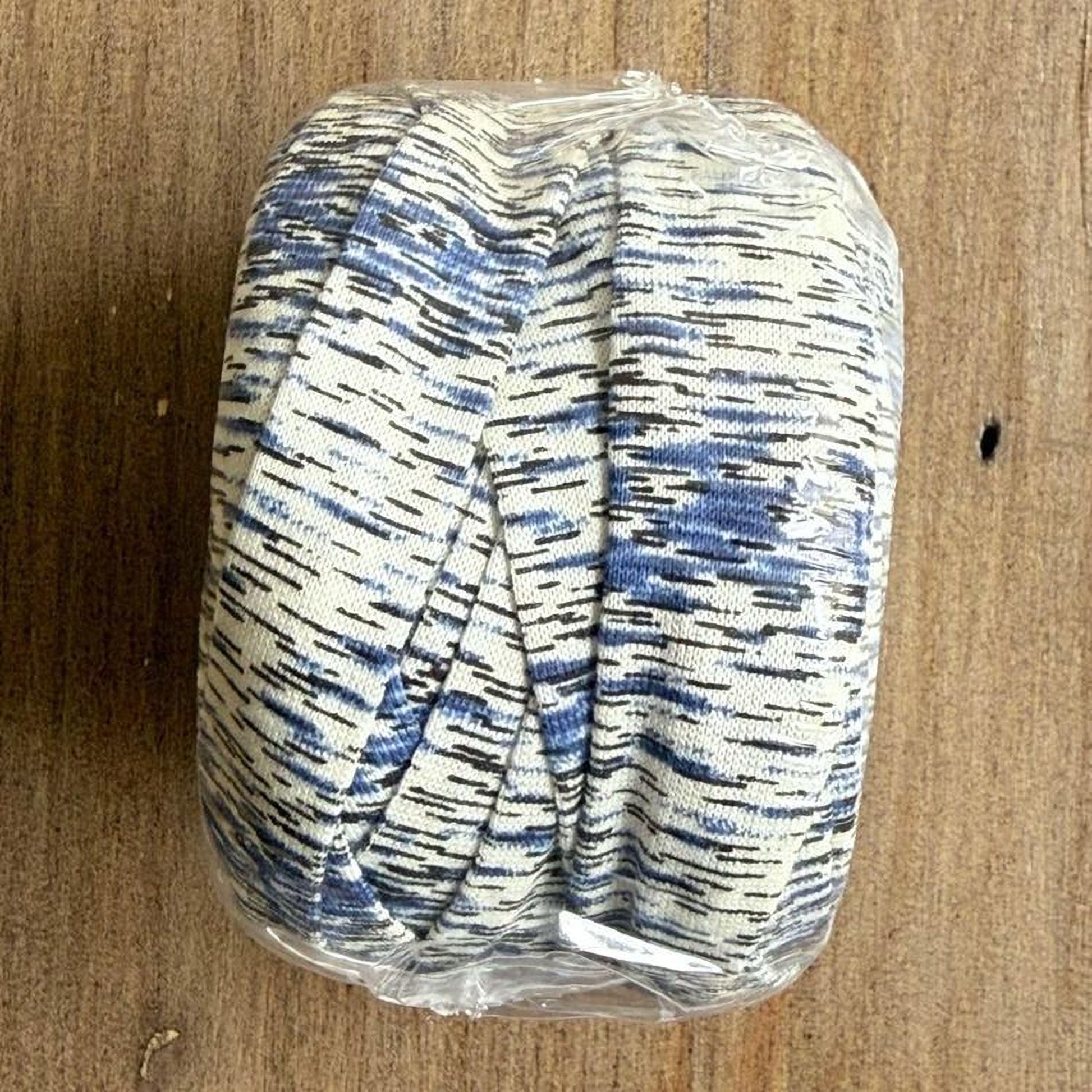 A roll of blue and white striped fabric is wrapped in plastic and placed on a wooden surface.