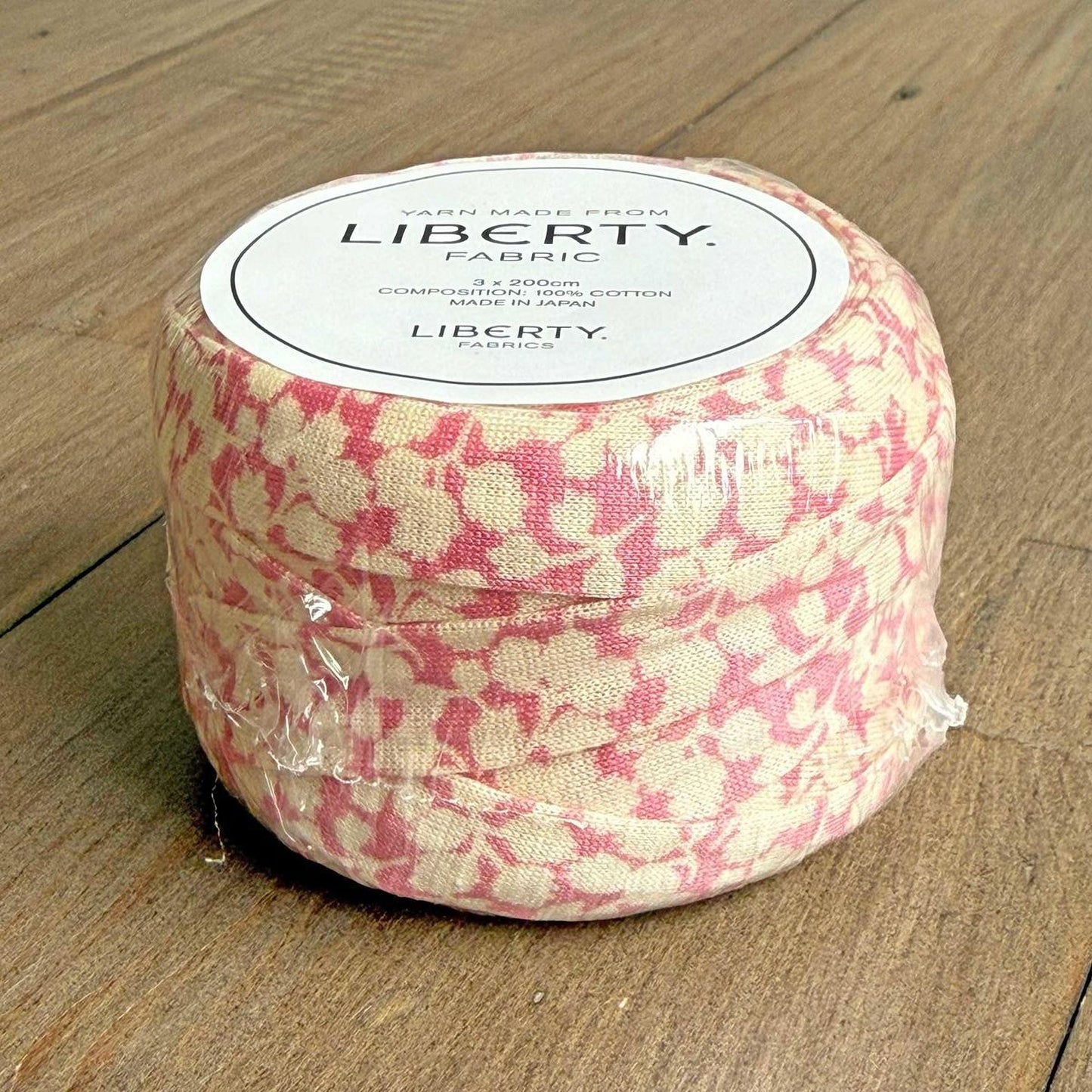 A package of Liberty fabric, which is a type of fabric, is sitting on a wooden surface.