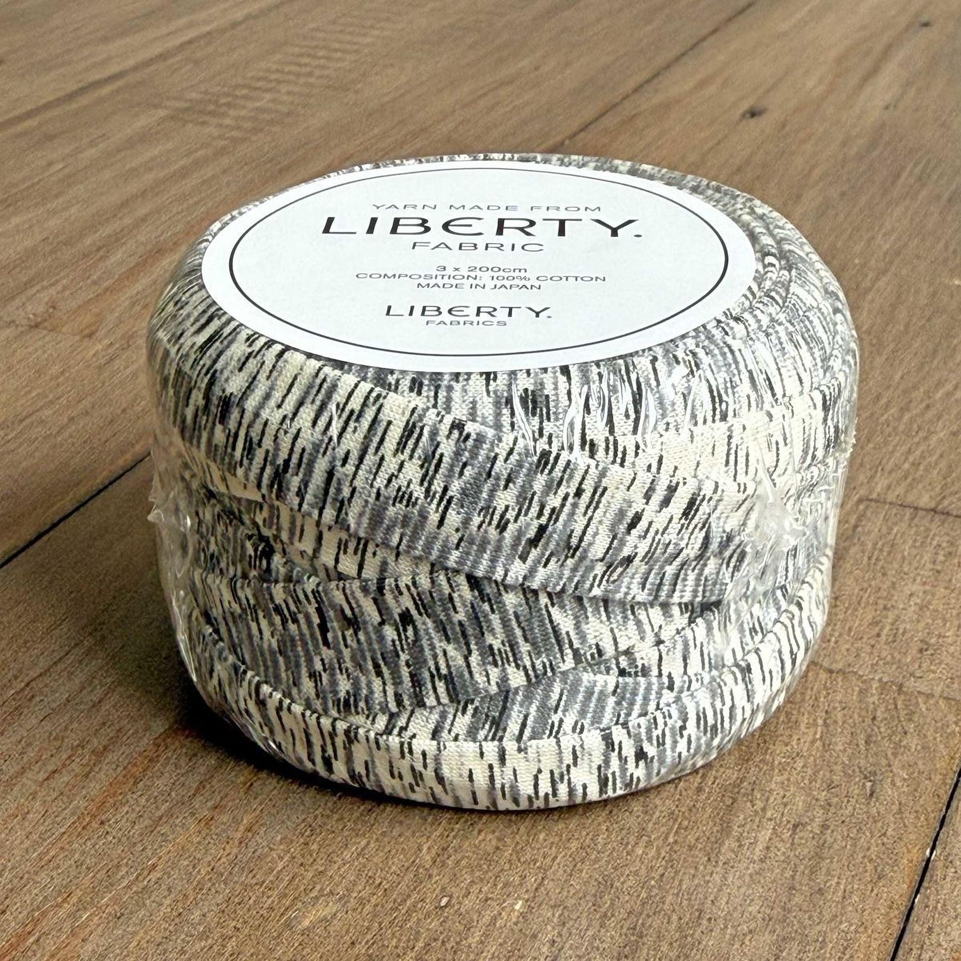 A spool of yarn with a textured pattern, sitting on a wooden surface.