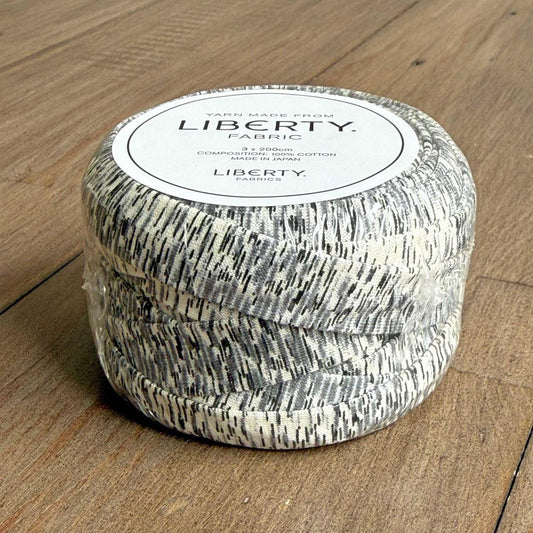 A spool of yarn with a textured pattern, sitting on a wooden surface.