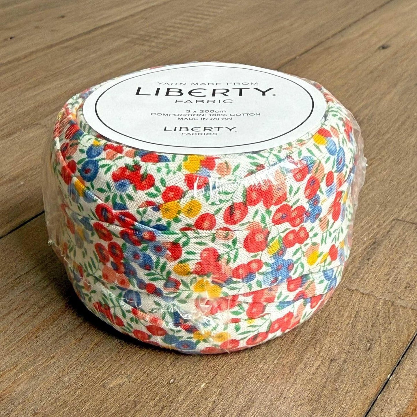A package of Liberty fabric, featuring a colorful floral pattern, is sitting on a wooden surface.