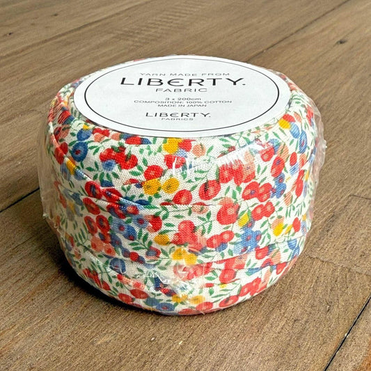 A package of Liberty fabric, featuring a colorful floral pattern, is sitting on a wooden surface.