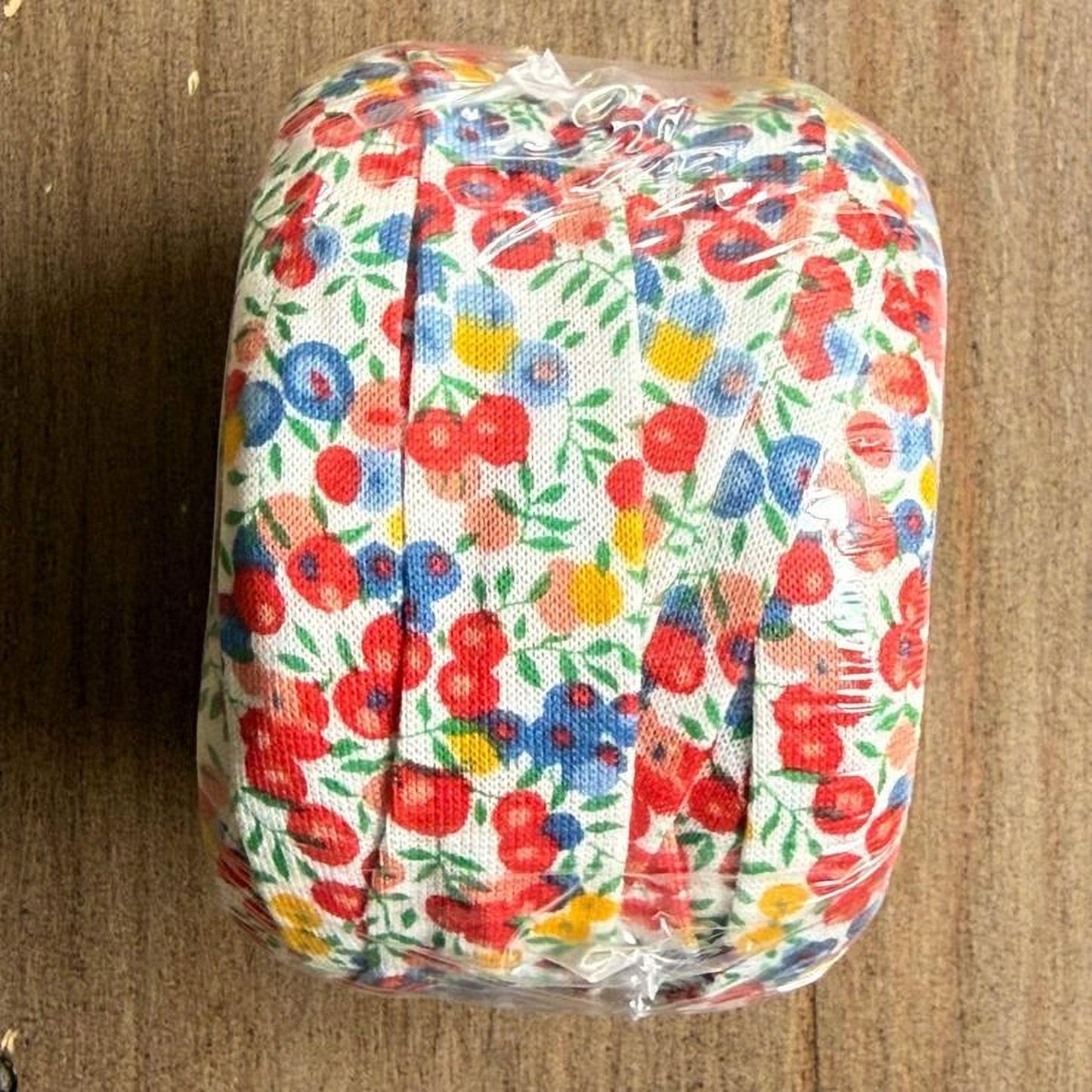 A roll of colorful floral fabric is wrapped in plastic and placed on a wooden surface.