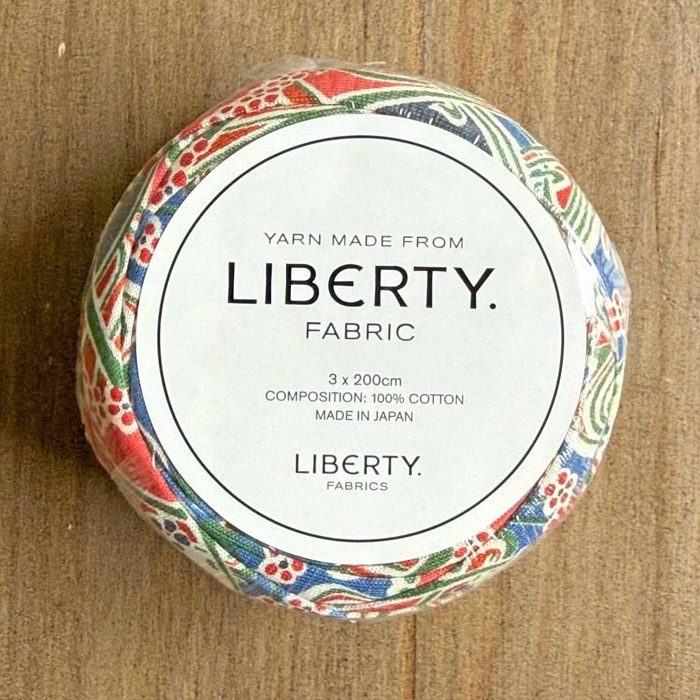 A circular object with a label that reads "Yarn Made from LIBERTY. FABRIC" and "3 x 200cm COMPOSITION: 100% COTTON MADE IN JAPAN LIBERTY FABRICS".