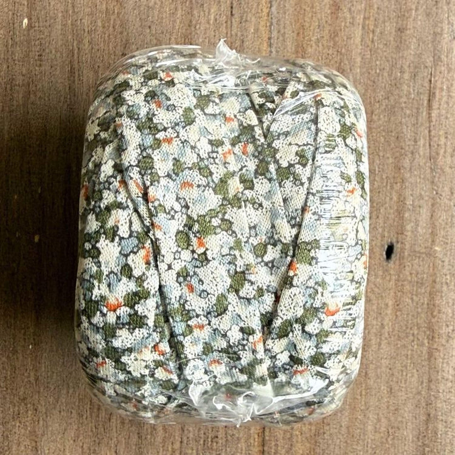 A package of fabric with a floral pattern, wrapped in plastic and placed on a wooden surface.