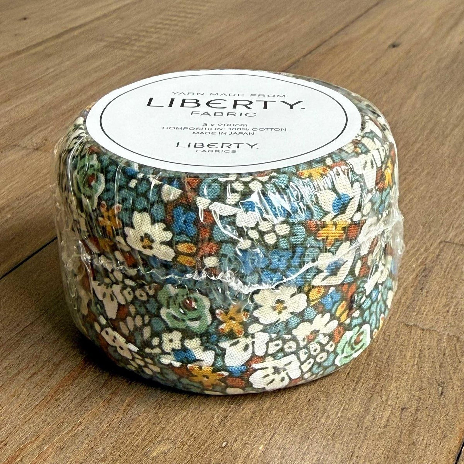 A package of Liberty fabric, featuring a floral print, is sitting on a wooden surface.