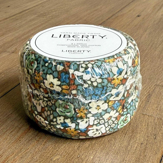A package of Liberty fabric, featuring a floral print, is sitting on a wooden surface.
