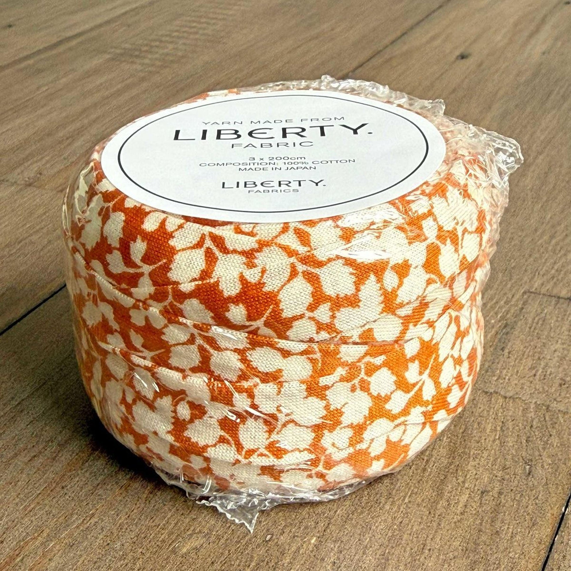 A package of Liberty fabric, featuring a floral pattern in shades of orange and white.