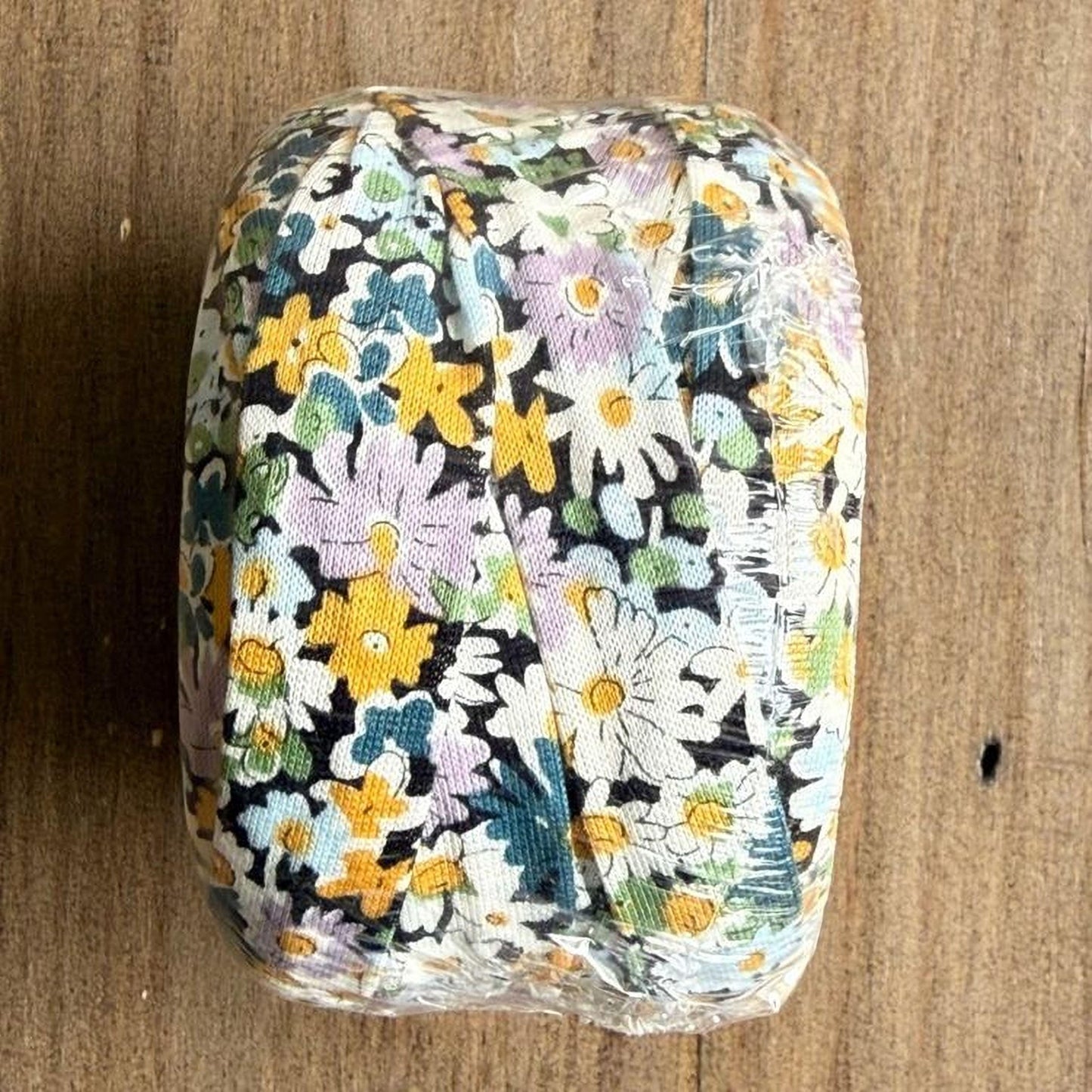 A floral patterned object, possibly a piece of fabric or paper, is wrapped in plastic and placed on a wooden surface.