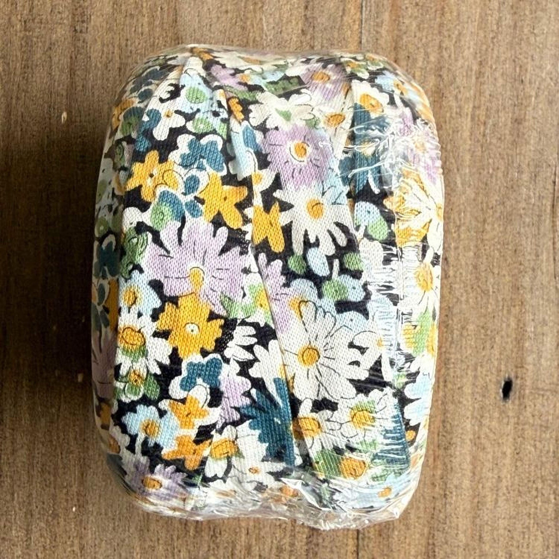 A floral patterned object, possibly a piece of fabric or paper, is wrapped in plastic and placed on a wooden surface.