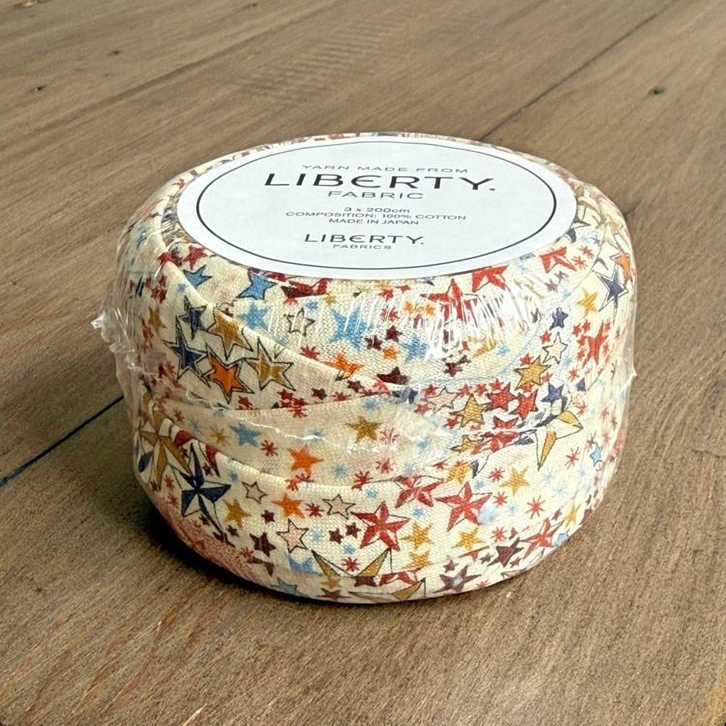 A package of Liberty fabric, featuring a colorful star-patterned design, is sitting on a wooden surface.