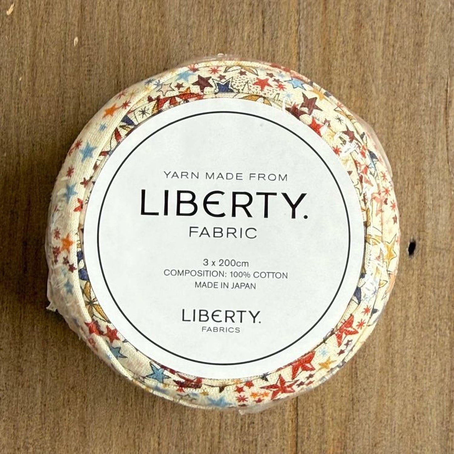 A circular object with a white label that reads "Yarn Made from LIBERTY. FABRIC 3 x 2000cm COMPOSITION: 100% COTTON MADE IN JAPAN LIBERTY. FABRICS".