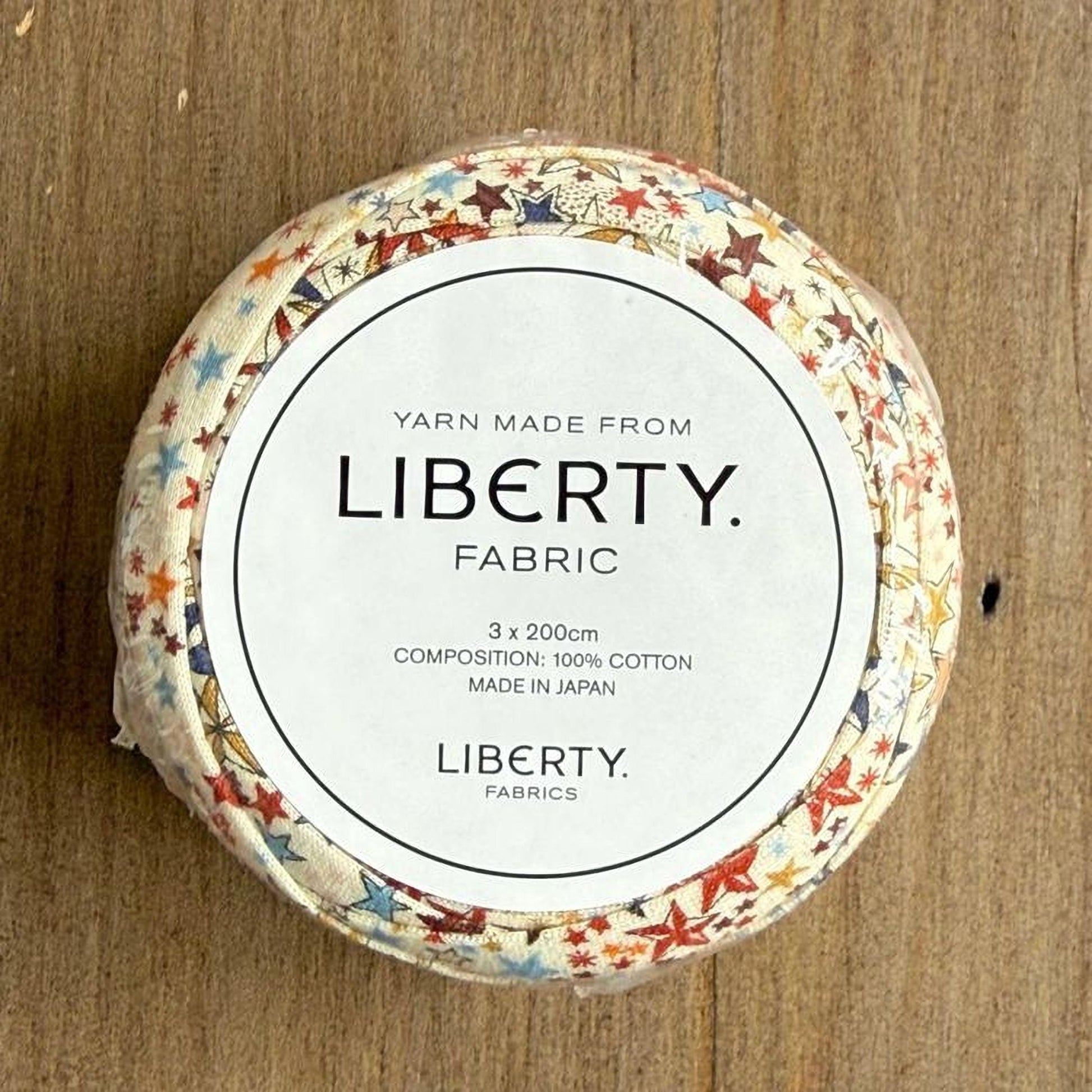 A circular object with a white label that reads "Yarn Made from LIBERTY. FABRIC 3 x 2000cm COMPOSITION: 100% COTTON MADE IN JAPAN LIBERTY. FABRICS".