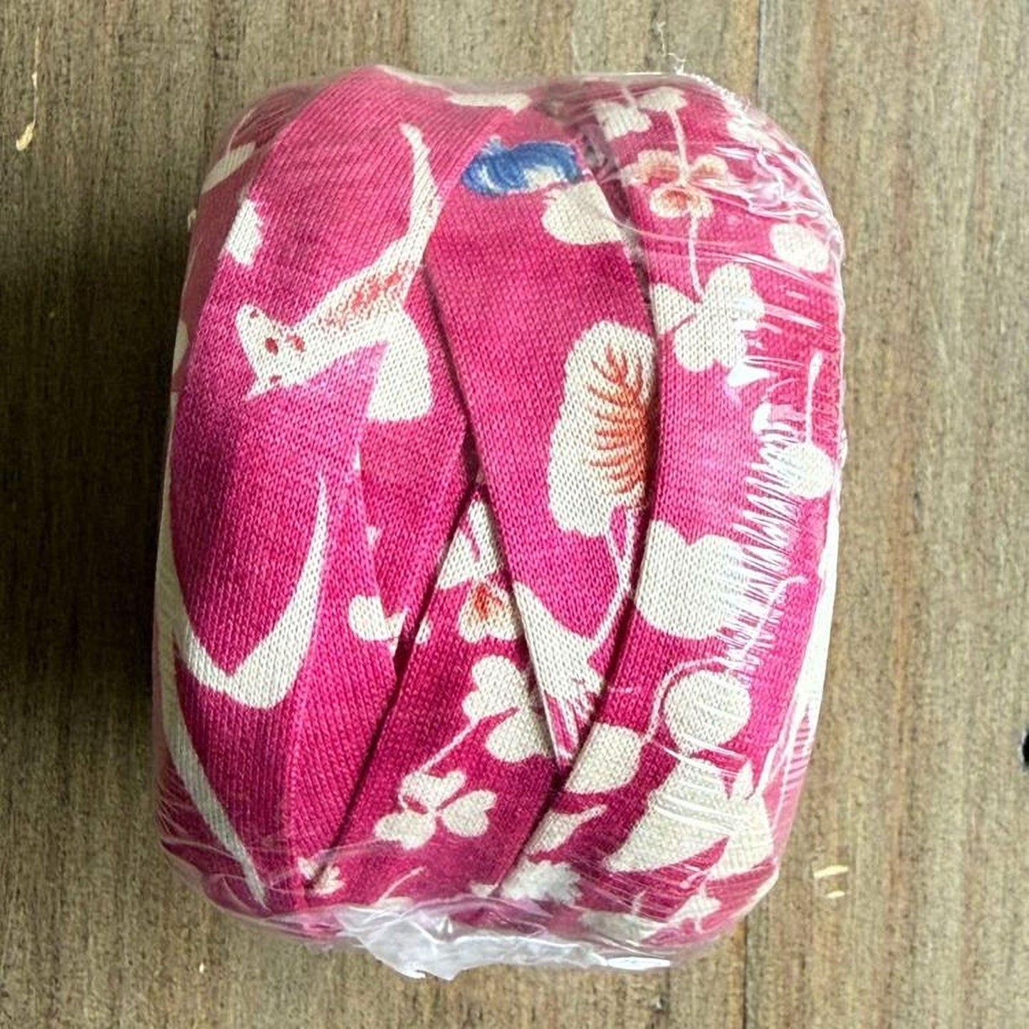 A pink fabric with white floral patterns is wrapped in plastic and placed on a wooden surface.