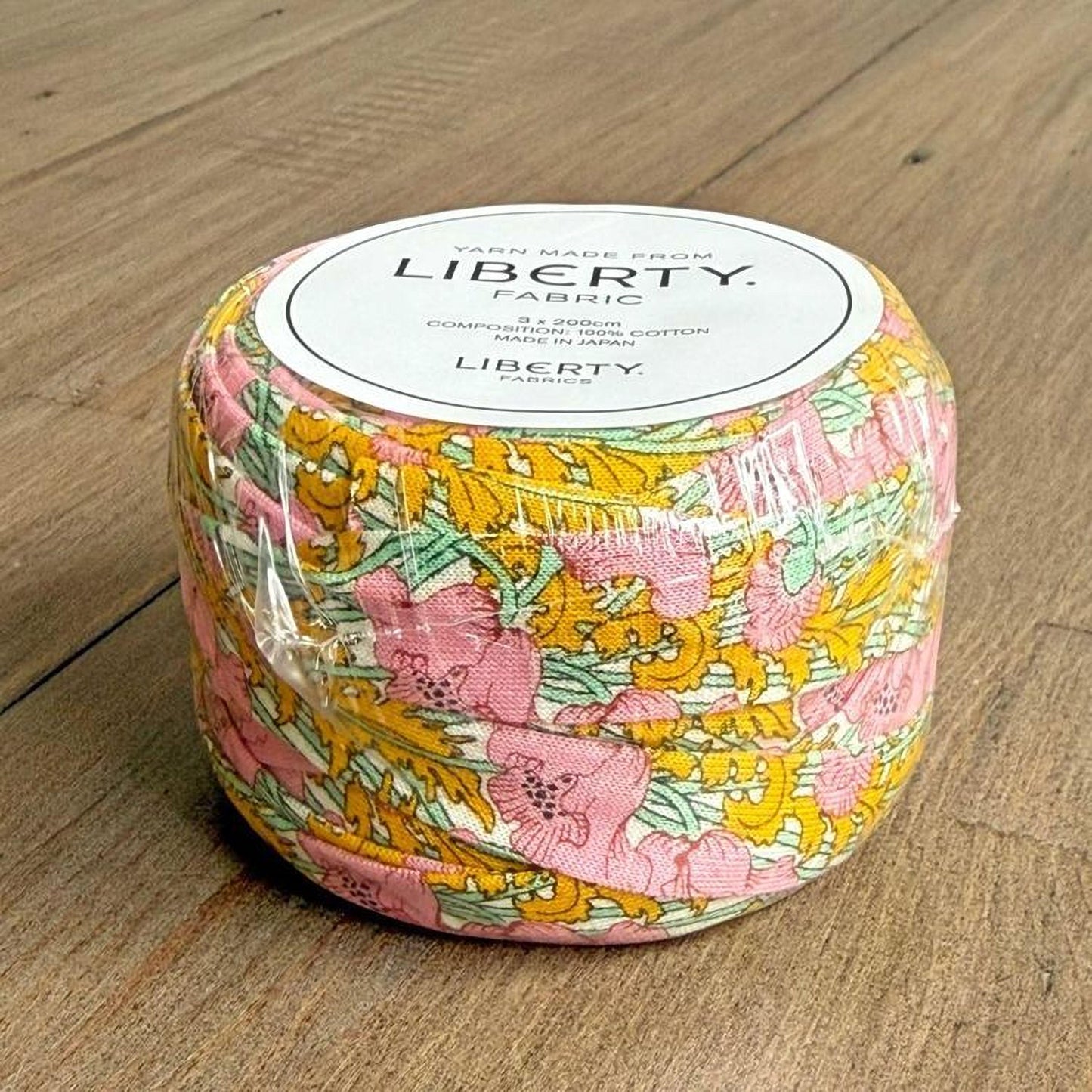 A package of fabric spools with a floral print design, sitting on a wooden surface.