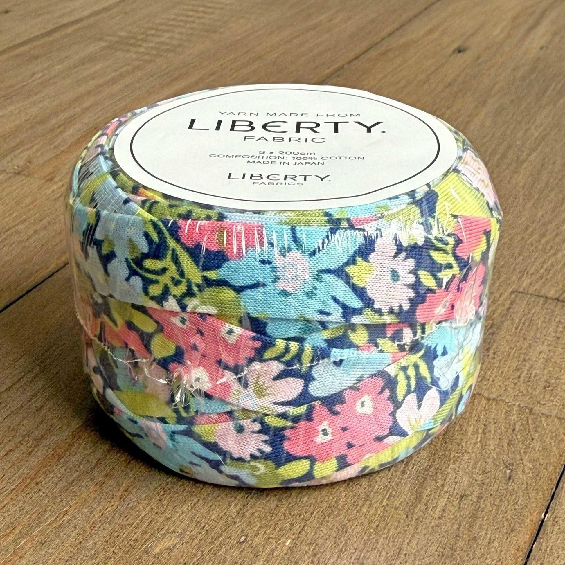 A package of Liberty fabric, featuring a colorful floral pattern, is sitting on a wooden surface.