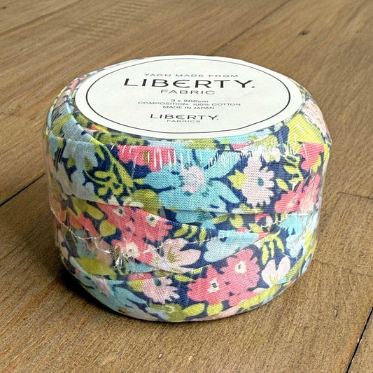 A package of Liberty fabric, featuring a colorful floral pattern, is sitting on a wooden surface.