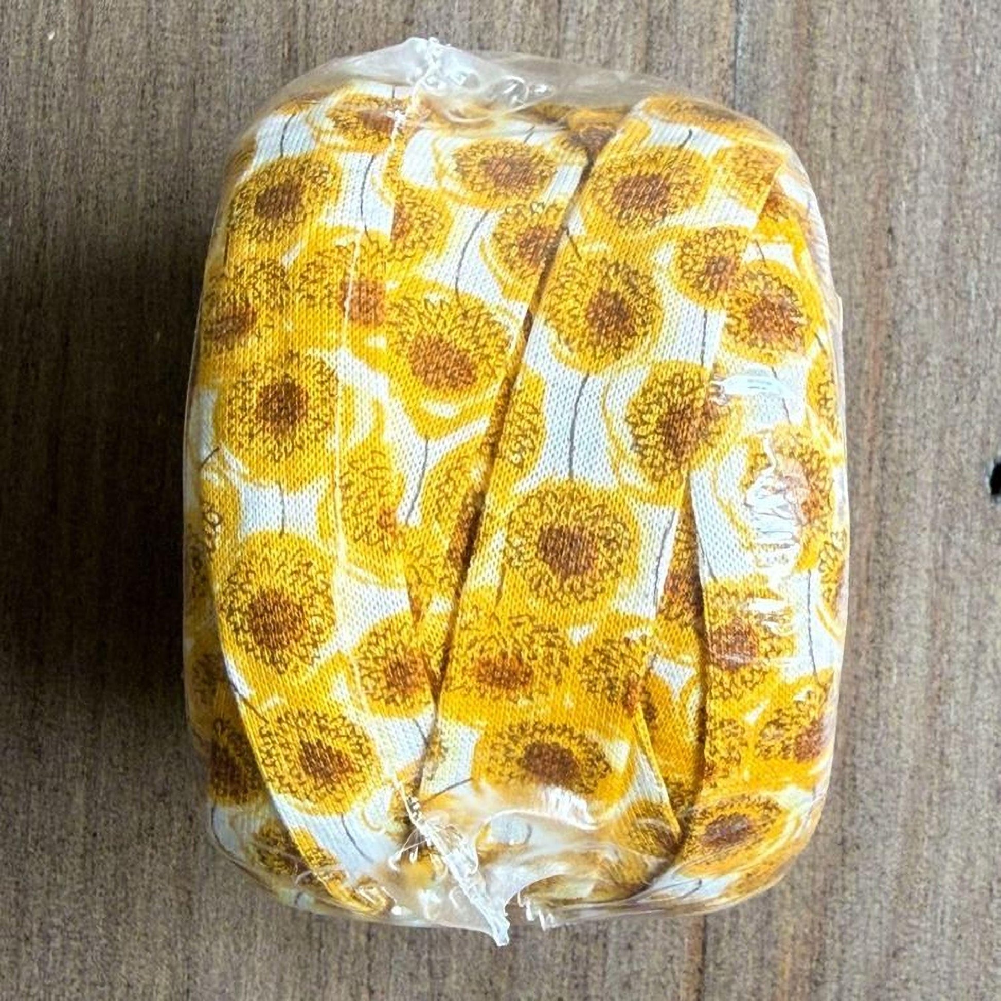 A roll of ribbon with a yellow and white floral pattern, sitting on a wooden surface.
