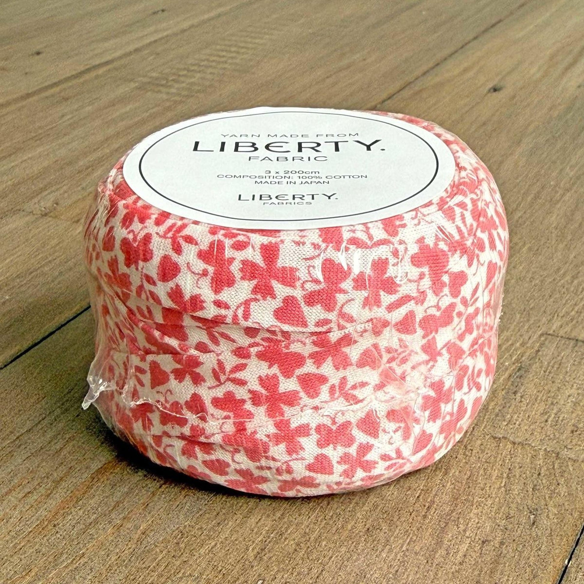 A package of fabric with a red and white floral pattern, sitting on a wooden surface.