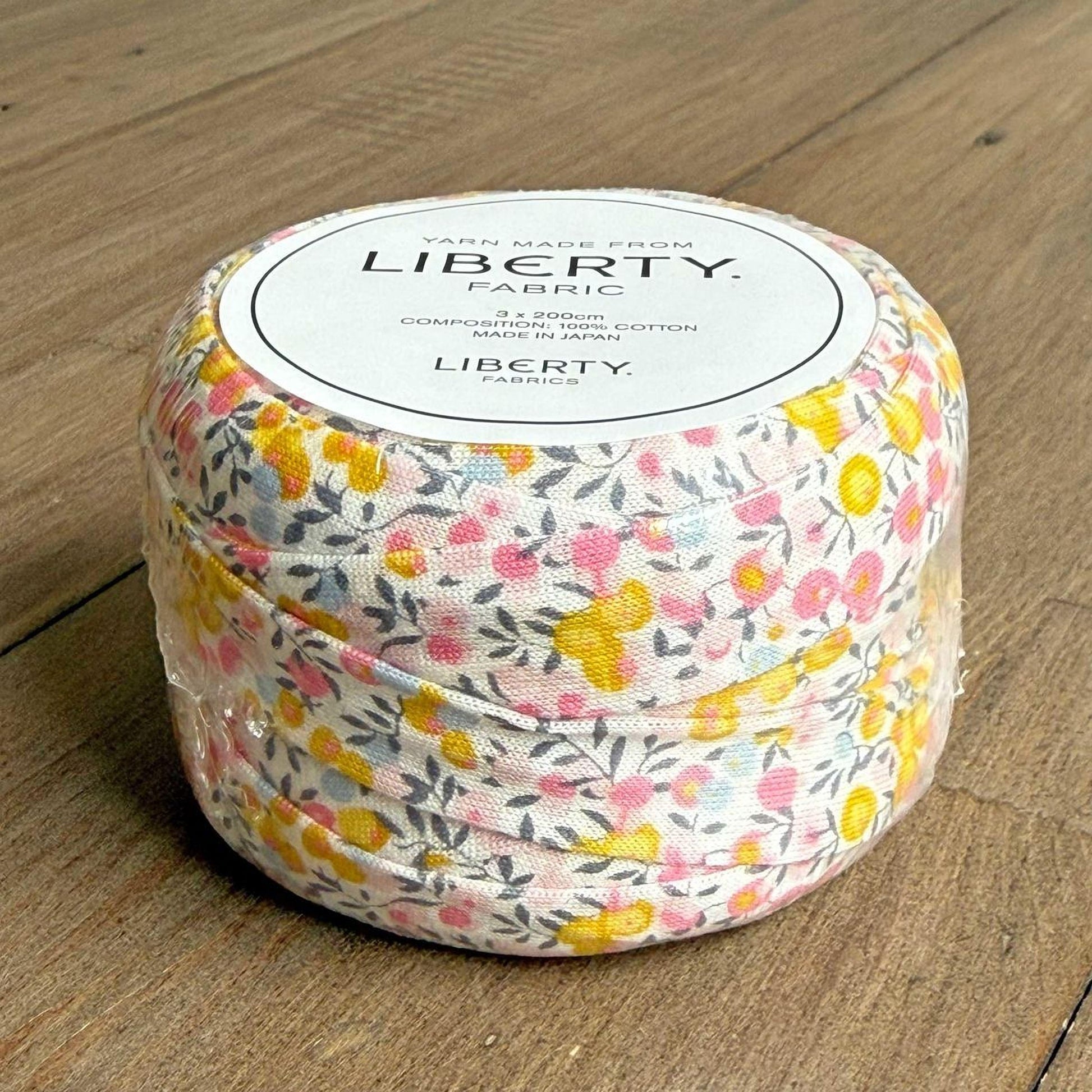 A spool of yarn with a floral print pattern is sitting on a wooden surface.