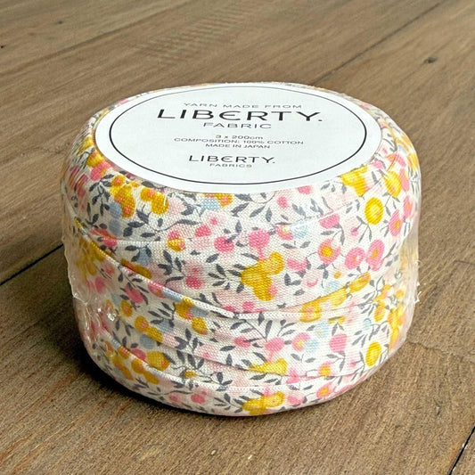 A spool of yarn with a floral print pattern is sitting on a wooden surface.