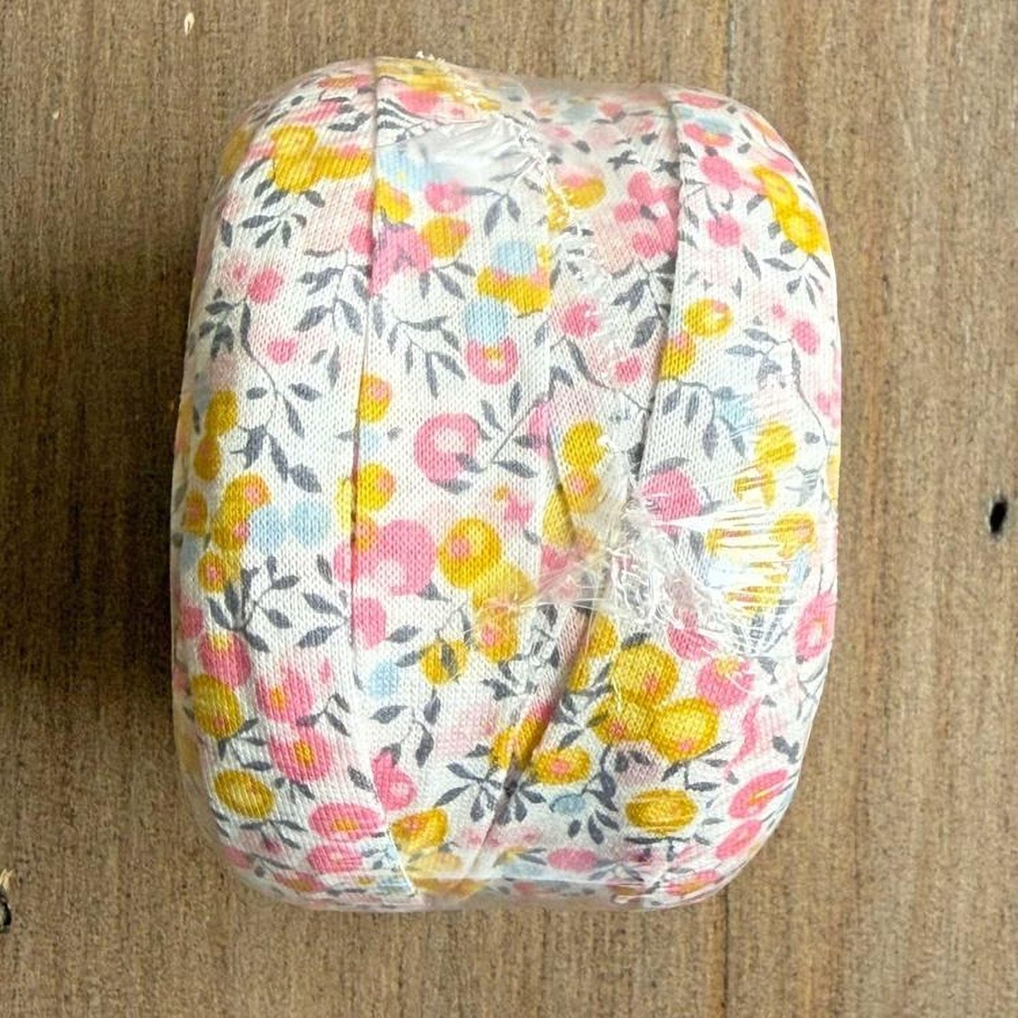 A white fabric with a floral pattern is wrapped in plastic and placed on a wooden surface.