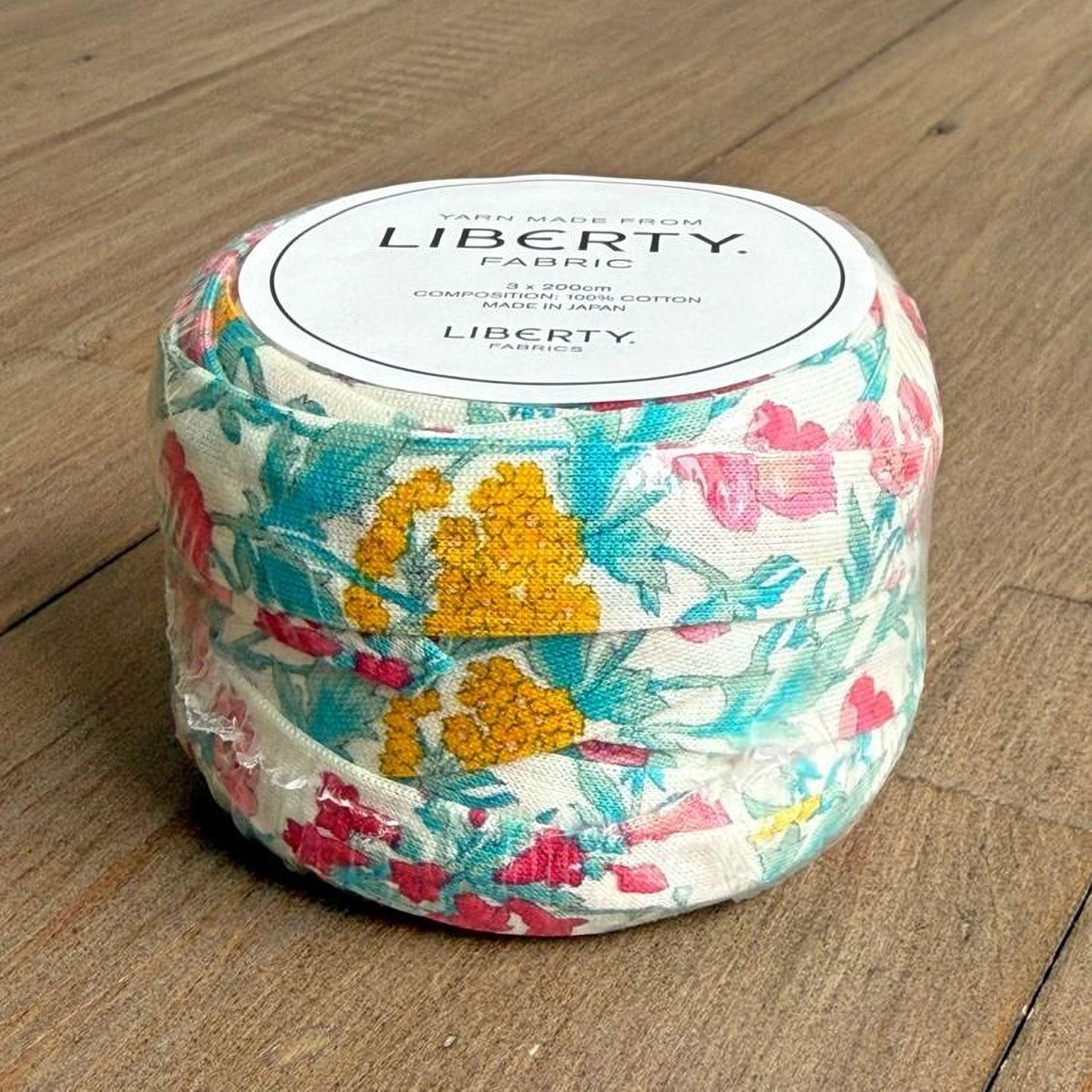 A package of fabric with a floral print design, sitting on a wooden surface.