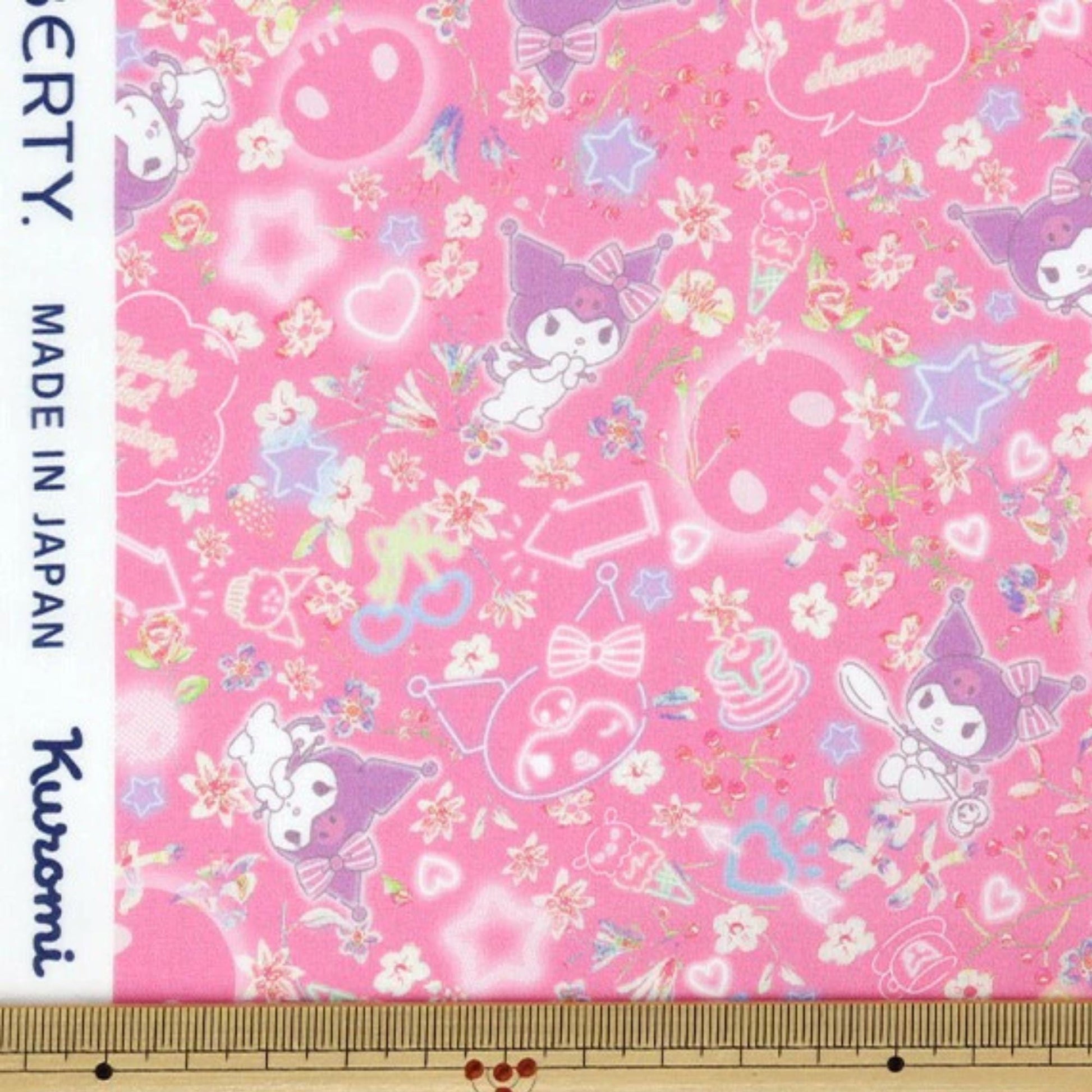The image is a fabric with a pink background and various cartoon-like characters, including a character wearing a hat and bow, as well as other whimsical elements.