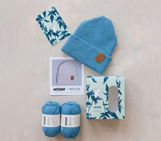 various knitting supplies, including yarn, a knit hat, and a box, arranged on a light-colored surface.