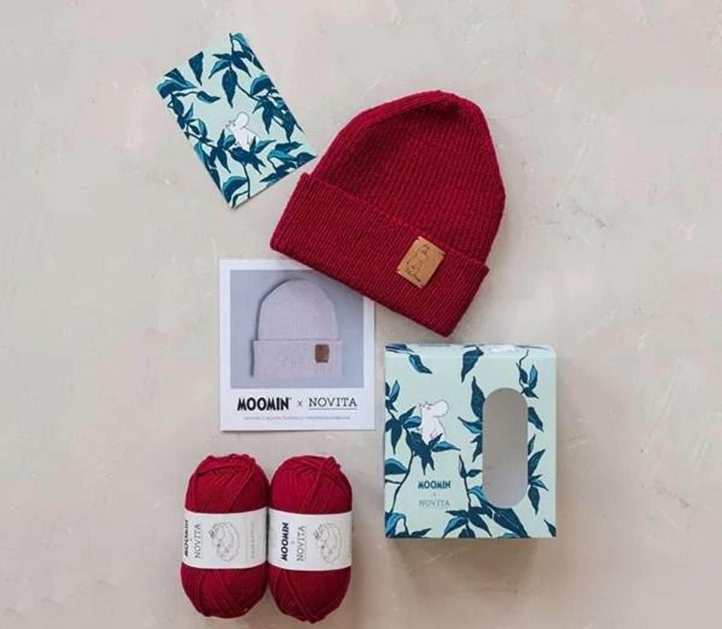 various knitwear items and yarn, including a red knit cap, two balls of yarn, and a box with a floral pattern.